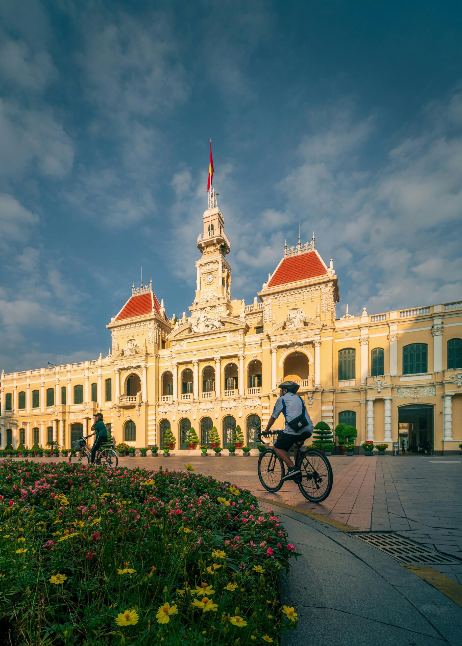 Bicyclists ride past the majestic Ho Chi Minh City Hall under a vibrant sky.